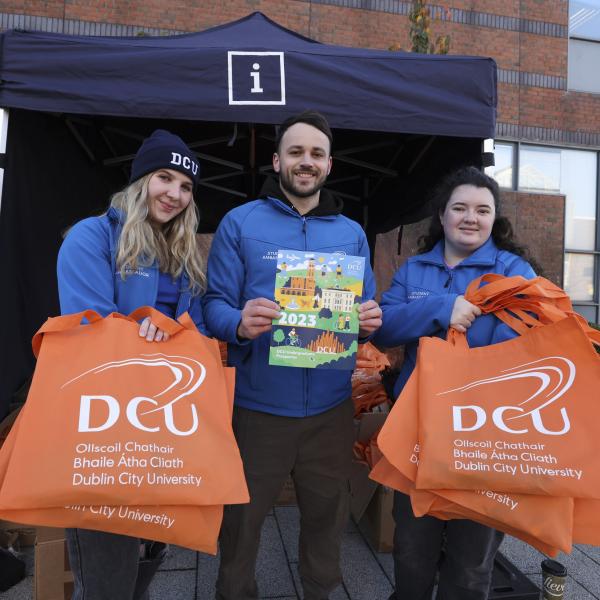 Shows three student ambassadors holidng bags and prospetus on DCU's Glasnevin campus