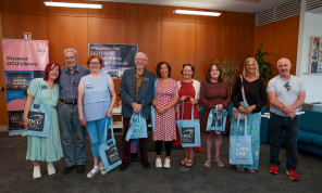 Nine people standing facing the camera holding blue bags