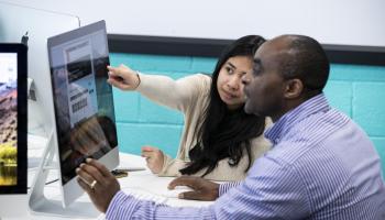 Picture of two students ( male and felmale) looking at a computer screen with the female student pointing at the screen