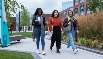 Image shows three students chatting and walking on campus
