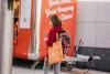 A young woman checking her phone while holding an orange DCU tote bag