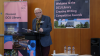 Shows a man reading from a lectern