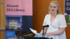 Shows a woman reading from a lectern