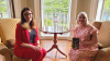 Shows two women sitting on chairs facing the camera. One woman is holding a book.