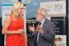 A woman in a red dress talks to a man in a suits who looks animated