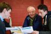 An older man is teaching two young men who are all reading a piece of paper