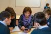 Three young men are gathered around an older woman who has her cellphone out and she is now looking at her phone