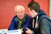 An older man is talking with a young man, they are discussing a paper that is in front of them 