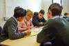 A group of young students are gather around an older woman who is teaching them 