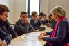 A group of young students are gathered around an older woman who is teaching them 