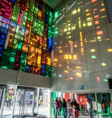 Sunshine pours through coloured glass windows reflecting the colours on concrete wall