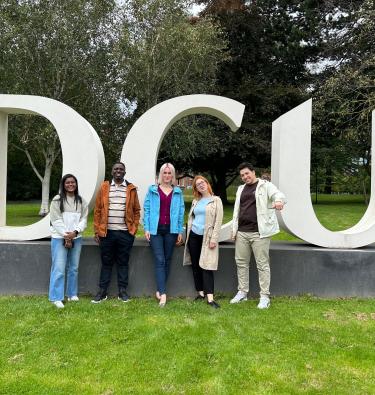 Shows some of the Sanctuary scholarship recipients standing in front of a DCU sign