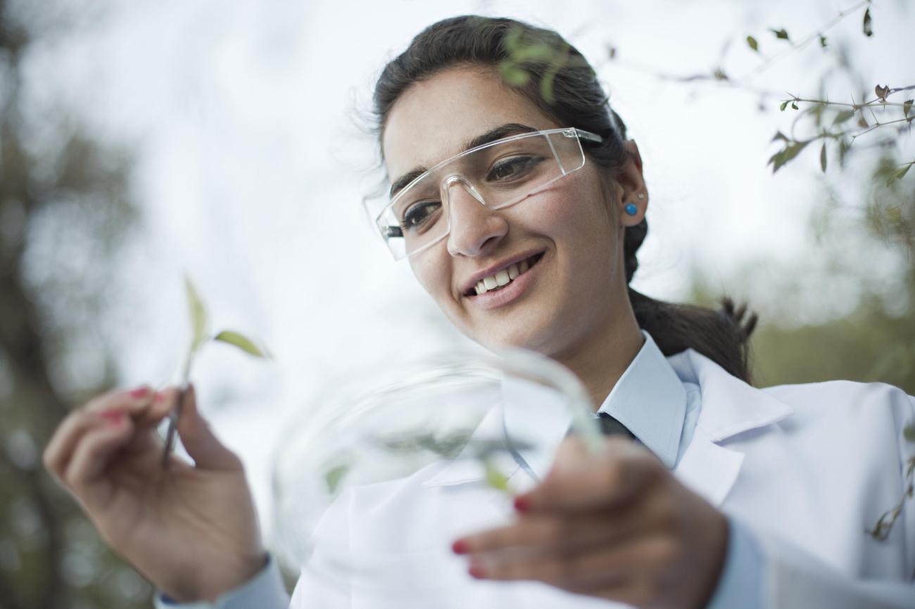 Student in lab coat with goggles and petri dish
