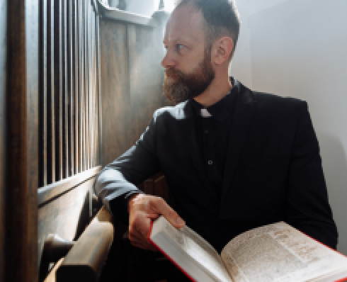 Shows a priest holding a book in a confessional box 