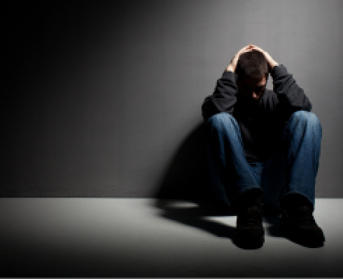 Shows a young man in a dark room sitting on the floor