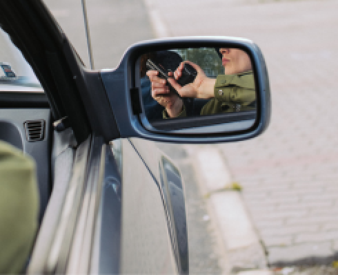 A man holding a gun sitting in a car is reflected in the car's side mirror