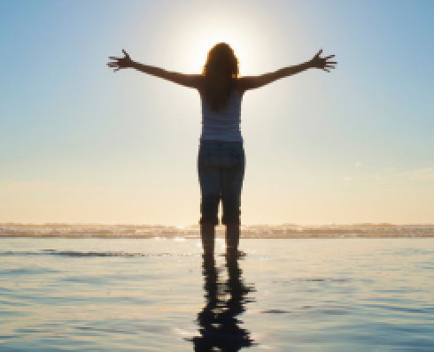 Shows a woman standing in water facing the sun with her arms stretched out