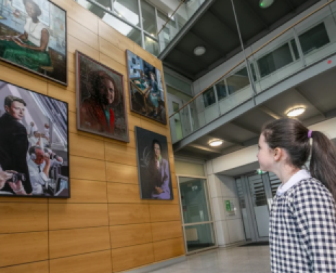 Young girl looks up at portraits of five women (Beatrice Alice Hicks, Katherine Johnson, Dame Kathleen Lonsdale, Marie Maynard Daly and Kathleen (Kay) McNulty) hung on a tall wooden wall 