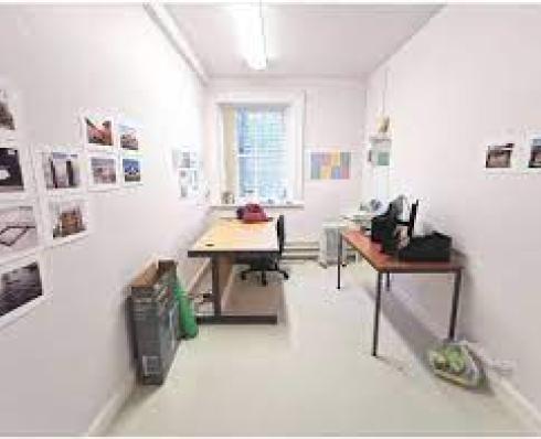 Artist studio with white walls, two desks, a window and some artwork hung on the wall 