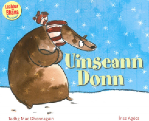 Graphic of a bear with a scarf who is standing on snow and hugging himself. Text on the page reads: Uinseann Donn, Tadhg Mac Dhonnagáin, Irisz Agócs, leabhar na bliana - shortlisted.