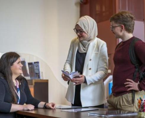 Staff member helping 2 students at the help desk in Woodlock hall library