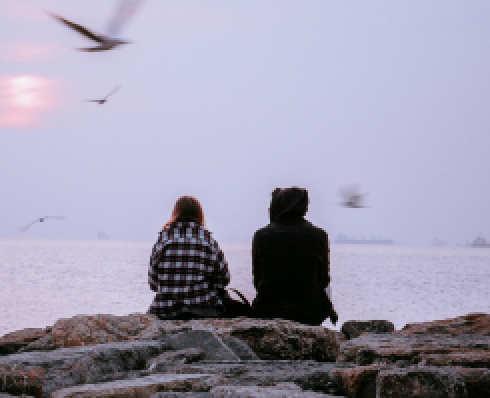 Two people sitting on the rocks looking out at the sea