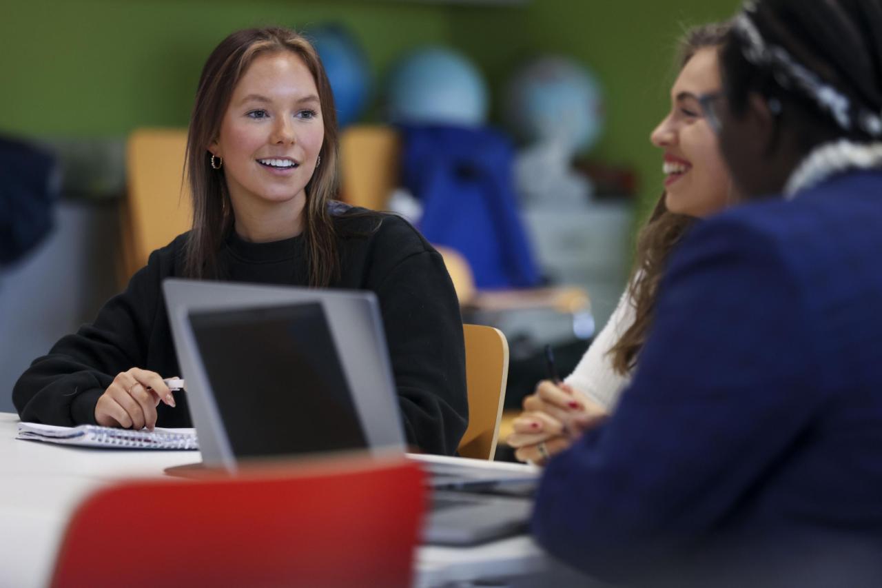 3 students talking at a desk with their laptops open