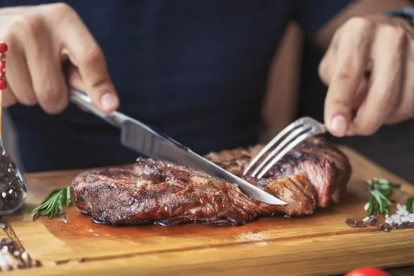 Shows man cutting up steak