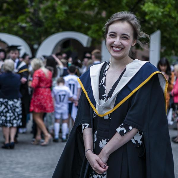 A woman poses for the camera, smiling widely, in a graduation cap and gown.