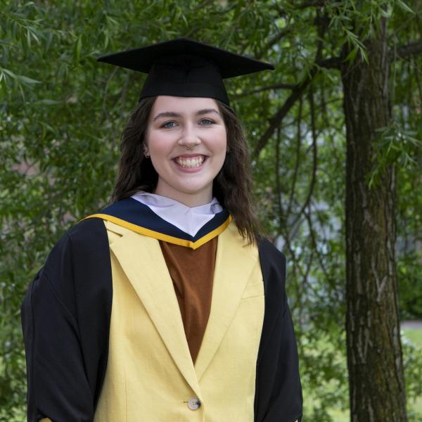 Sonja Tutty, recently graduated from a BA in Journalism, smiles for the camera in a graduation cap and gown.