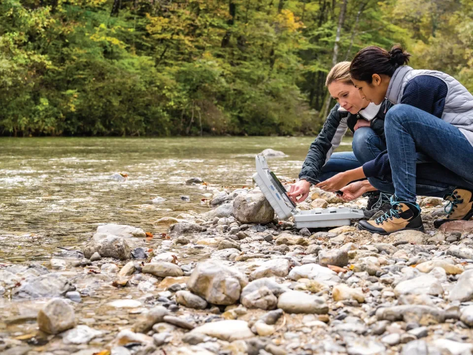 Two researchers by riverbed looking at laptop