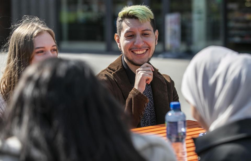 A photo of a group of international students, including Joao Luca Cavalheiro Camargo, sitting outside at an orange table smiling and talking