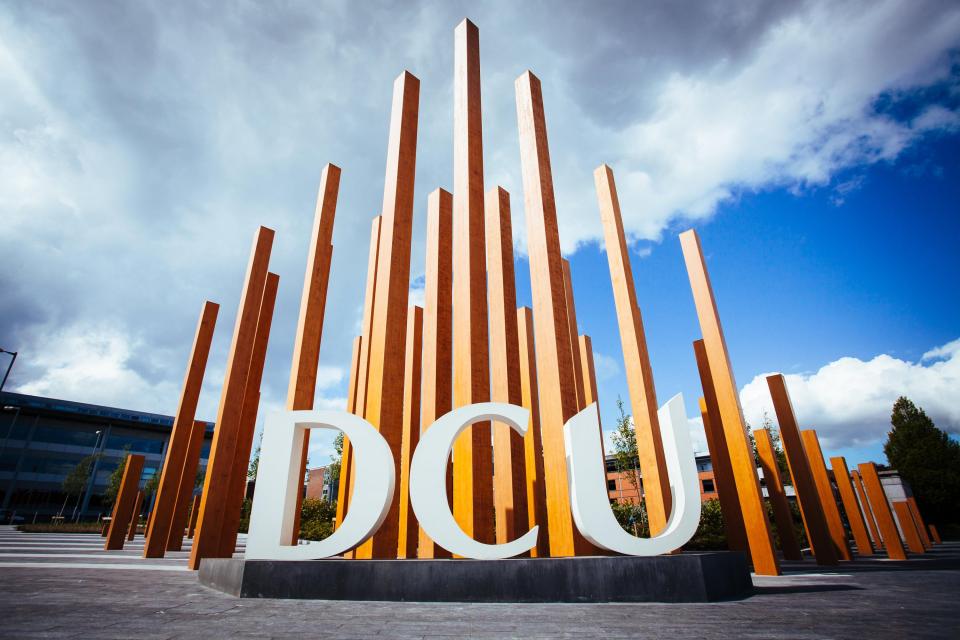 A photo of the DCU letters. In the background orange sticks pierce the sky.