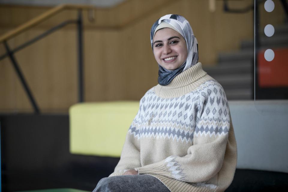 A woman in a headscarf wearing light coloured clothing sits on the coloured steps in the U, smiling to the camera.