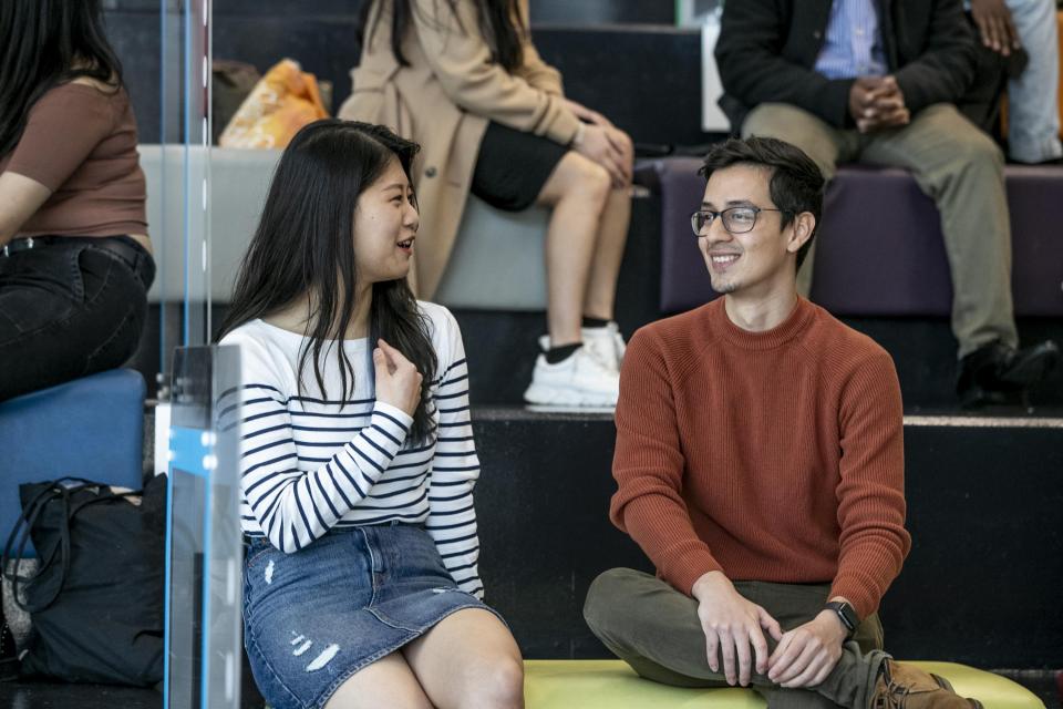 A photo of two international students talking in a group. They seem happy.