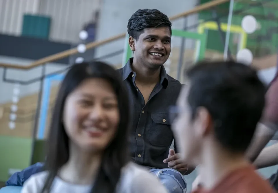 A photo of an Indian man talking to someone off camera. In the foreground an asian woman and a man talking, they are out of focus.