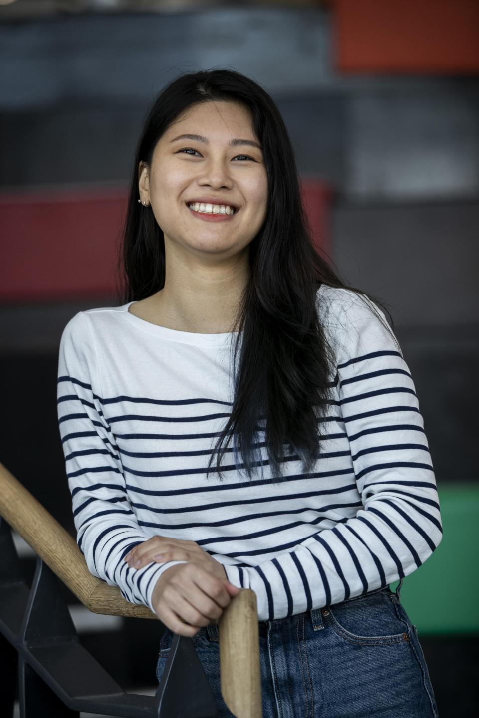 An Asian woman posing for the camera on a flight on stairs. She is wearing a white jumper and smiling to the camera.