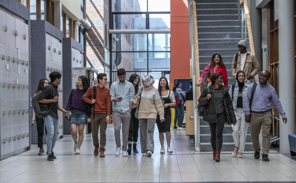 A group of international students, of all backgrounds and faiths, walking down a hallway chatting and laughing between themselves.