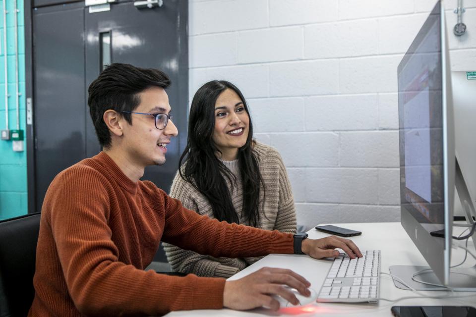 Two international students, sitting smiling in front of a computer.