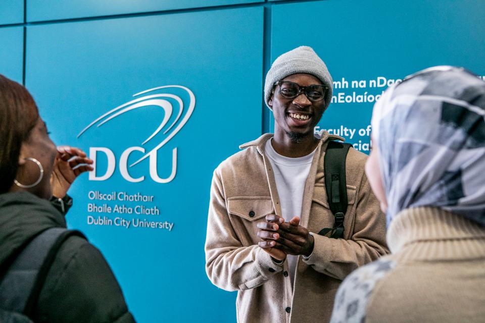 A group of students talking and laughing in front of a DCU sign.