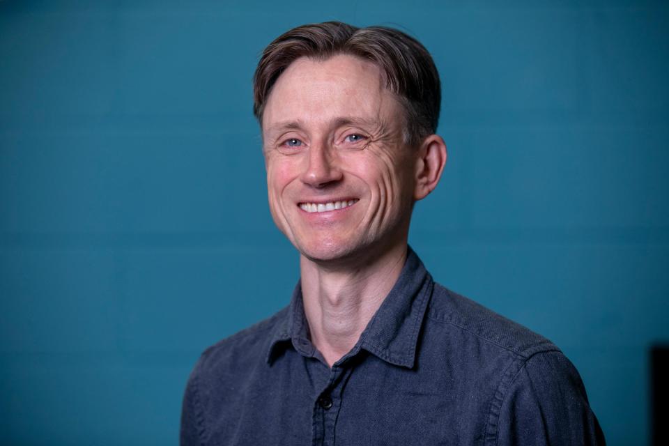 A professional headshot of a white man with short hair, wearing a navy shirt.