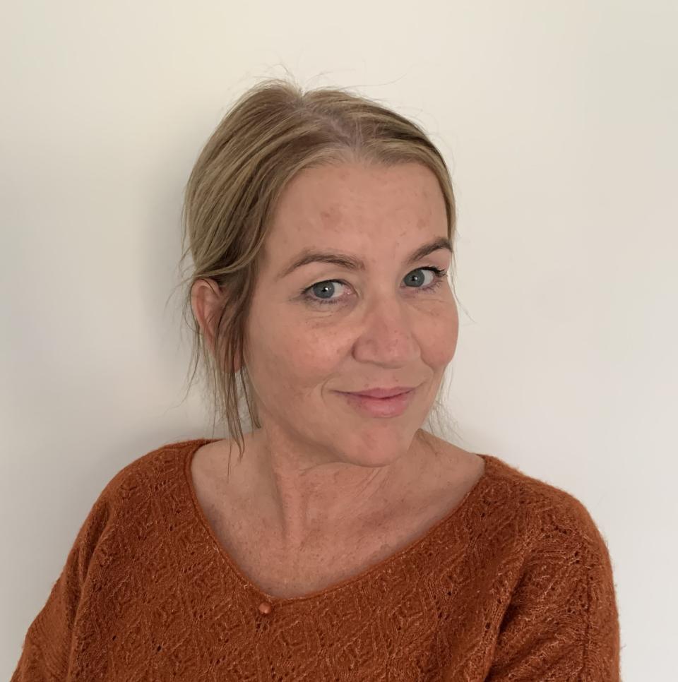 A photo of a woman with blonde hair wearing an orange jumper, smiling into the camera.