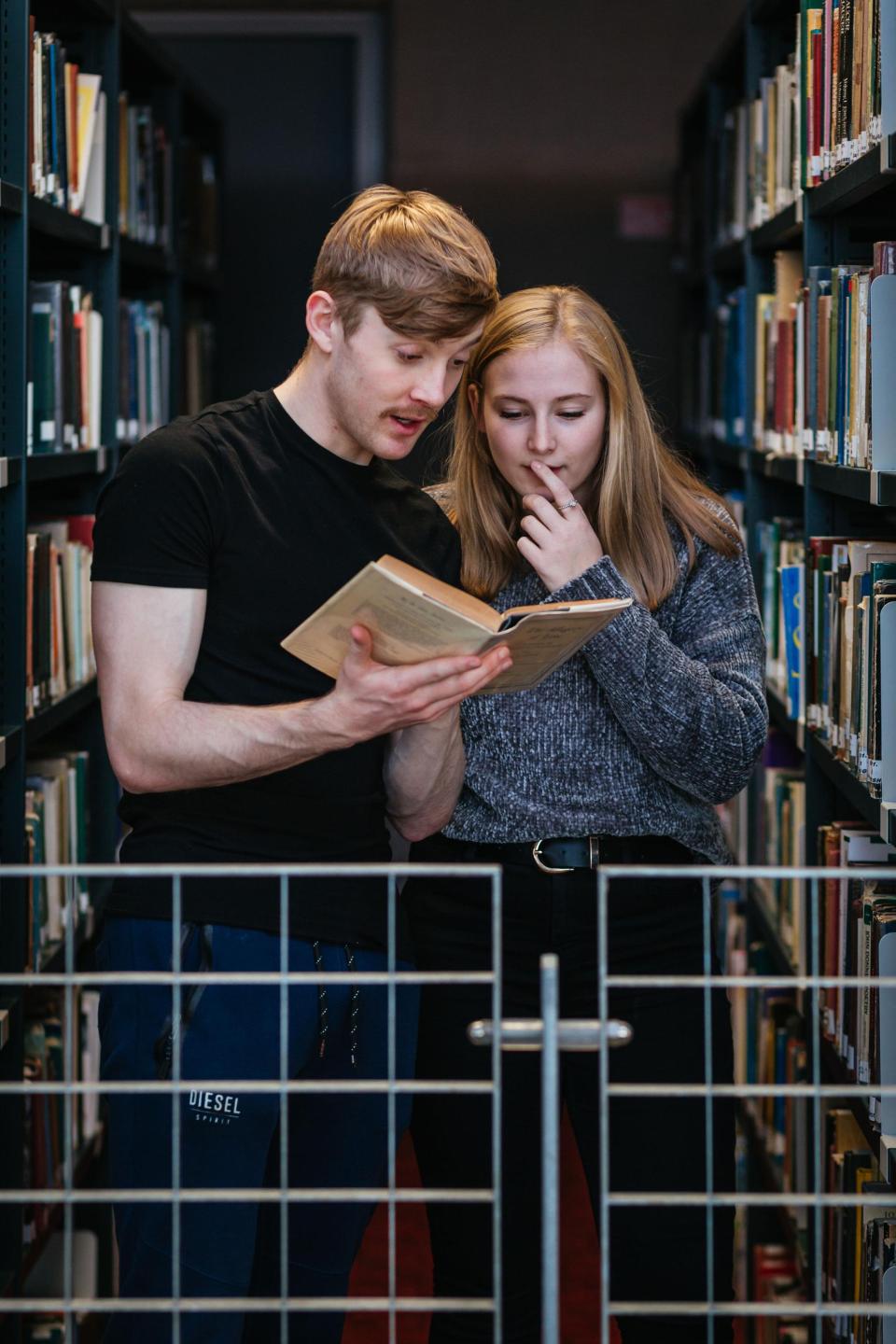 Two students reading a book in a library.
