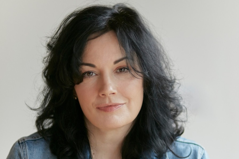 Aingeala Flannery - Writer in Residence. White skinned woman with black hair and brown eyes wearing a denim jacket stares down the lens of the camera