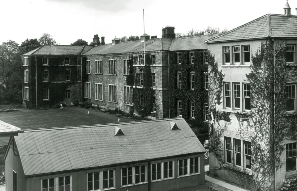 Black and white photo of Albert College, DCU - a large old bricked building covered in ivy