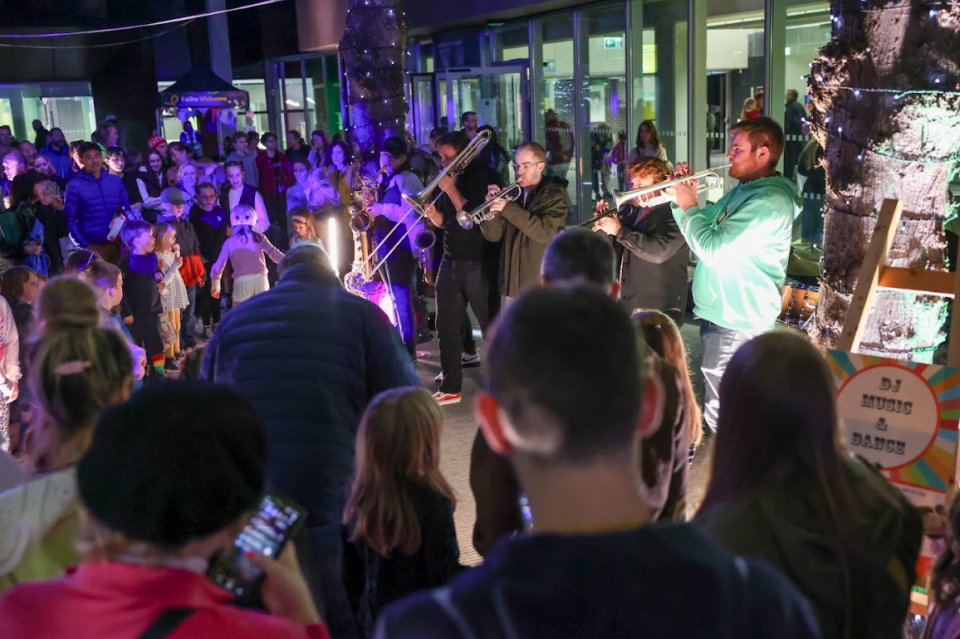 Audience gathered outside to watch an 8 piece brass band under purple lights
