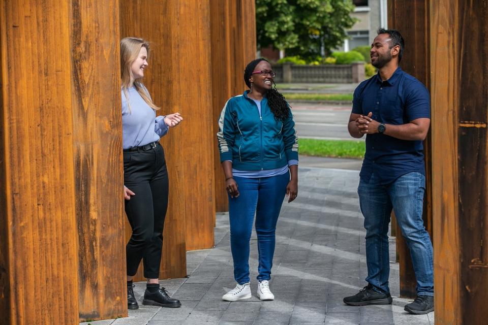 Three DCU students standing next to the DCU sign 