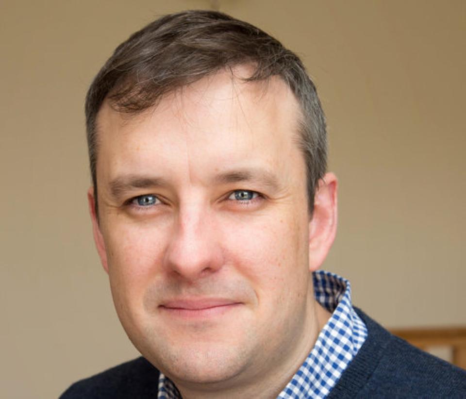 Photo of Andrew Kellett in a blue shirt and navy jumper.