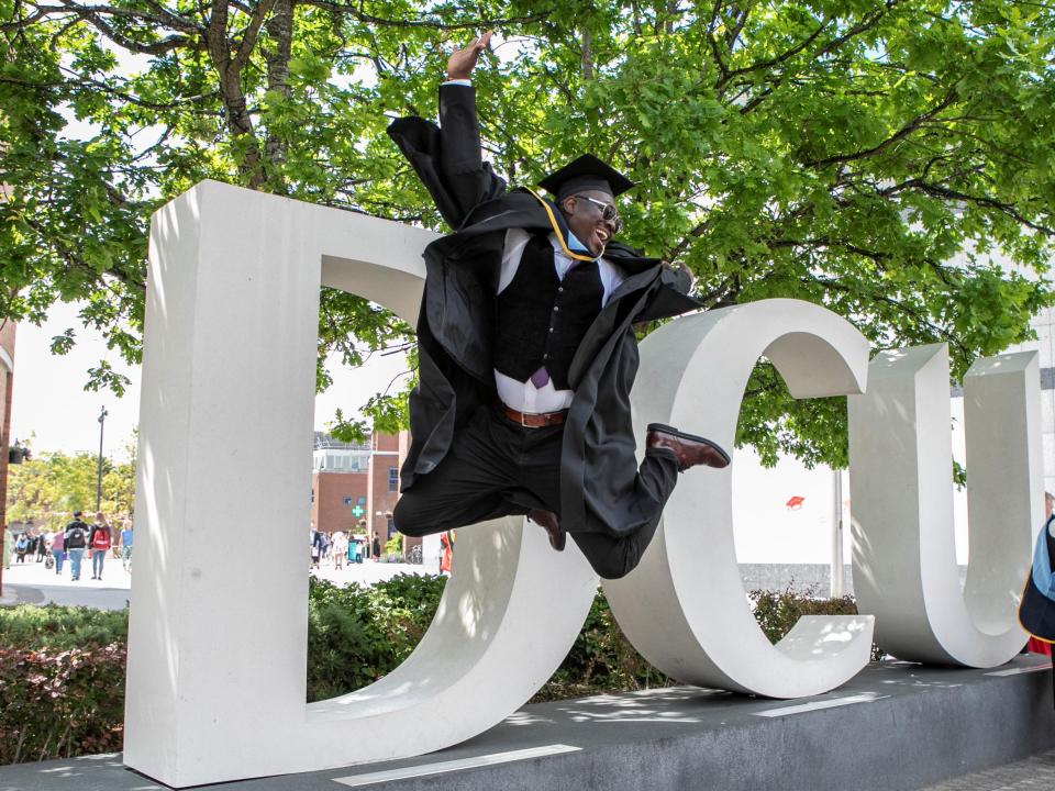 Male graduate leaps for joy at DCU letters