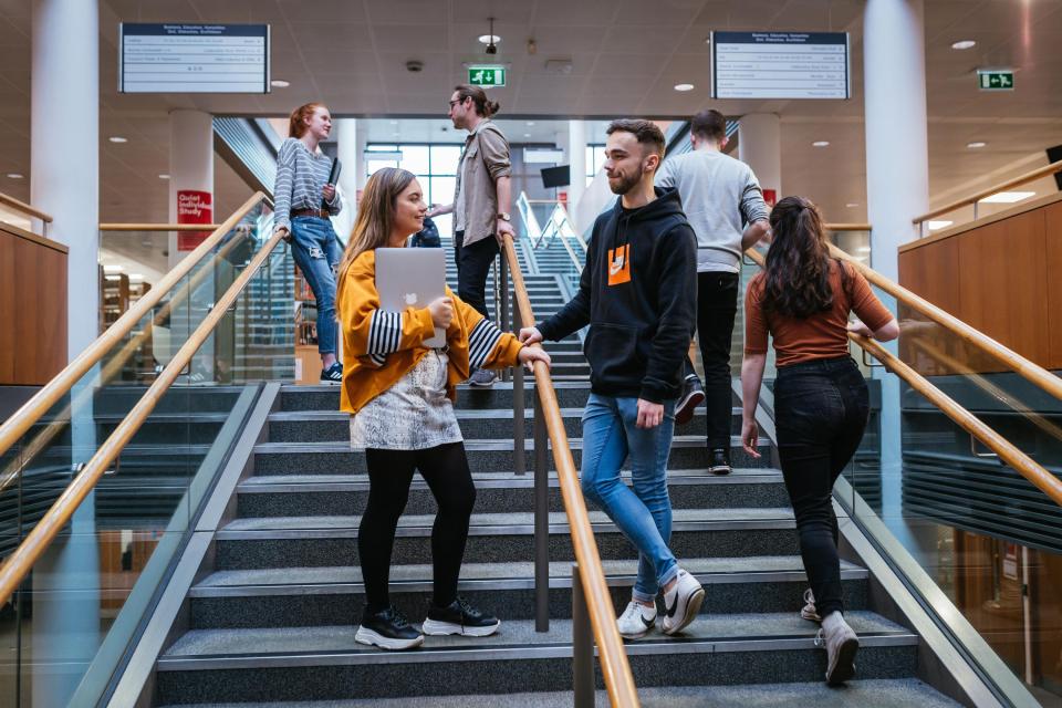 Four students stand talking on the staircase in O'Reilly Library as two other students climb the stairs.